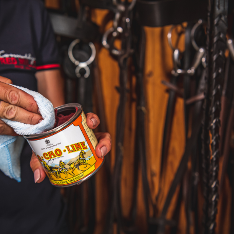 Person holding a can of Ko Cho Line leather dressing with a background of horse tack.