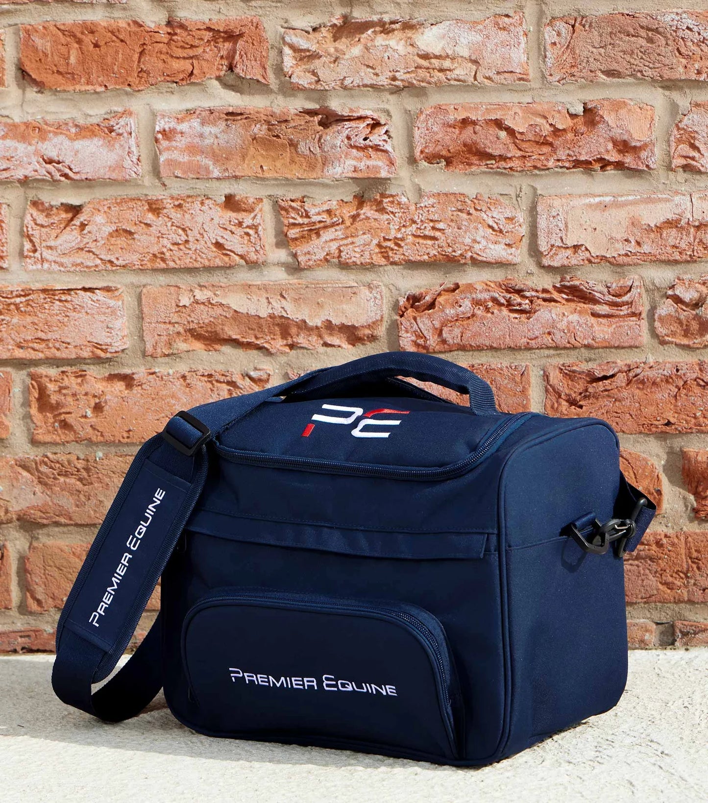 Navy blue grooming bag with 'Premier Equine' branding against a brick wall.