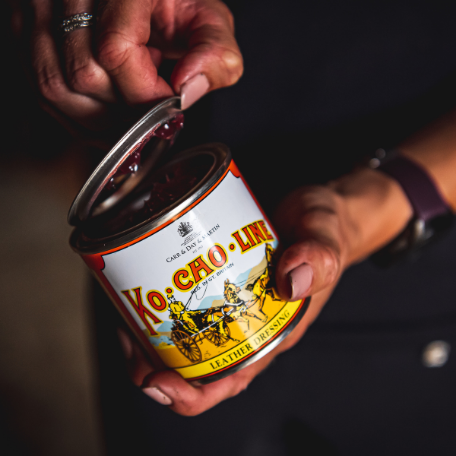 Hand holding a can of Ko Cho Line leather softening cream with a dark background