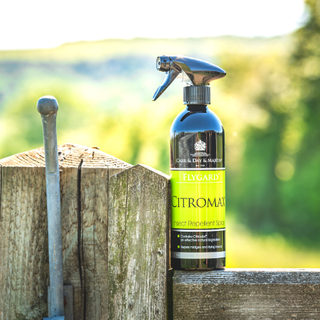 Citromax insect repellent spray bottle on a wooden post with a blurred natural background