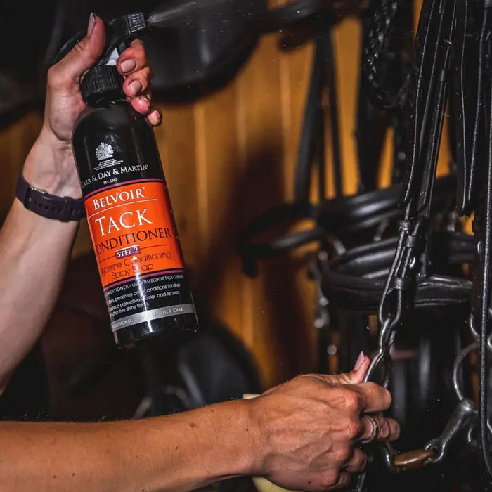Person holding a bottle of Belvoir Tack Conditioner next to horse tack.
