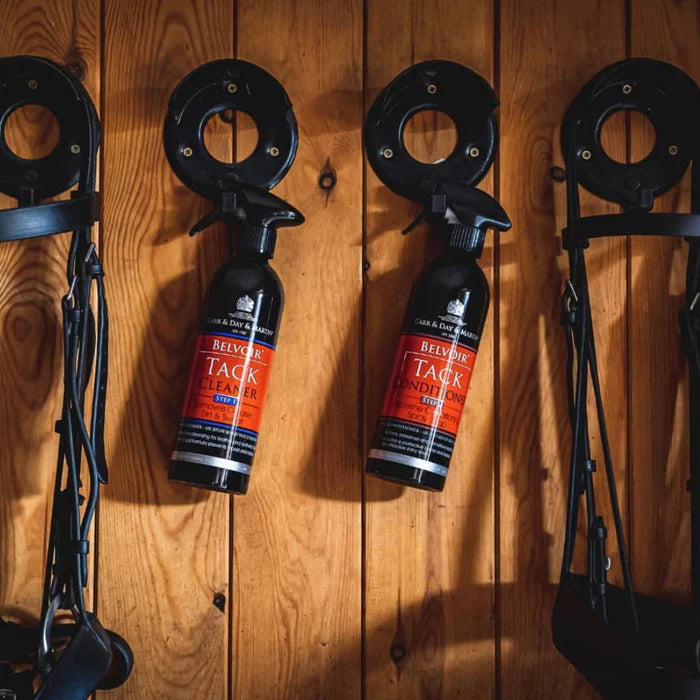 Two bottles of Belver Tack Lotion hanging on a wooden wall with horse tack equipment.