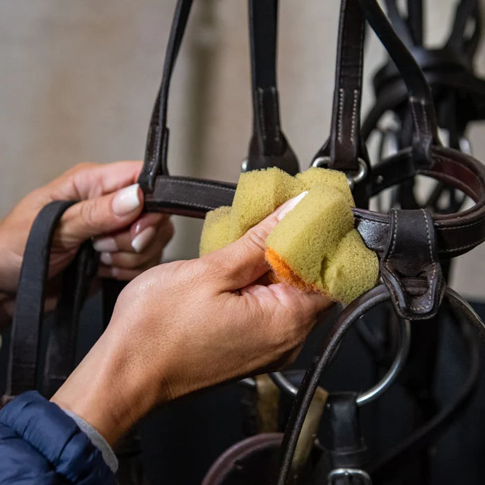 Person cleaning horse tack with a yellow sponge.
