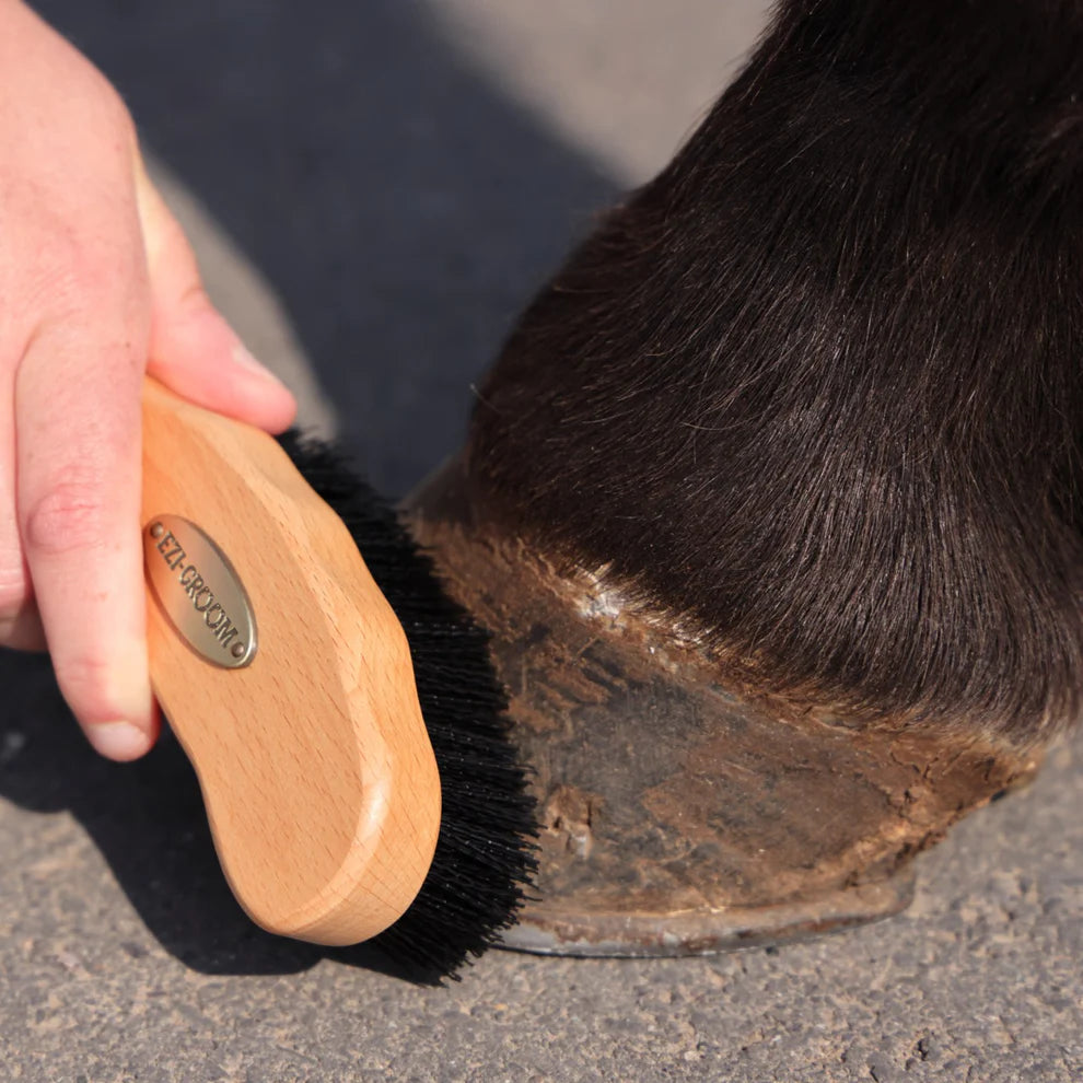 Person using a wooden horse brush on a horse's hoof.