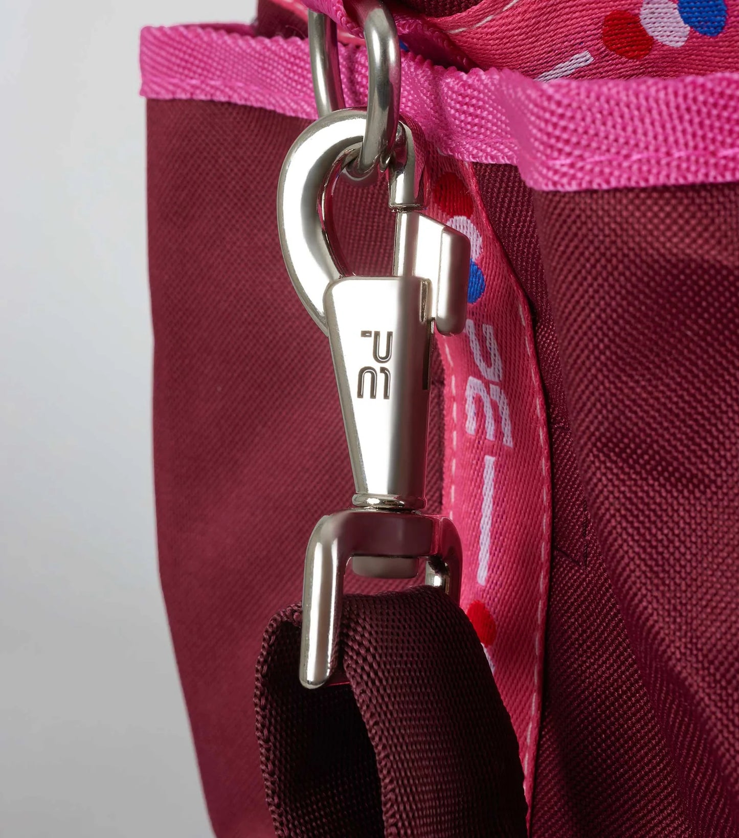 Close-up of a grooming bag with a metal clasp and pink strap featuring a logo.