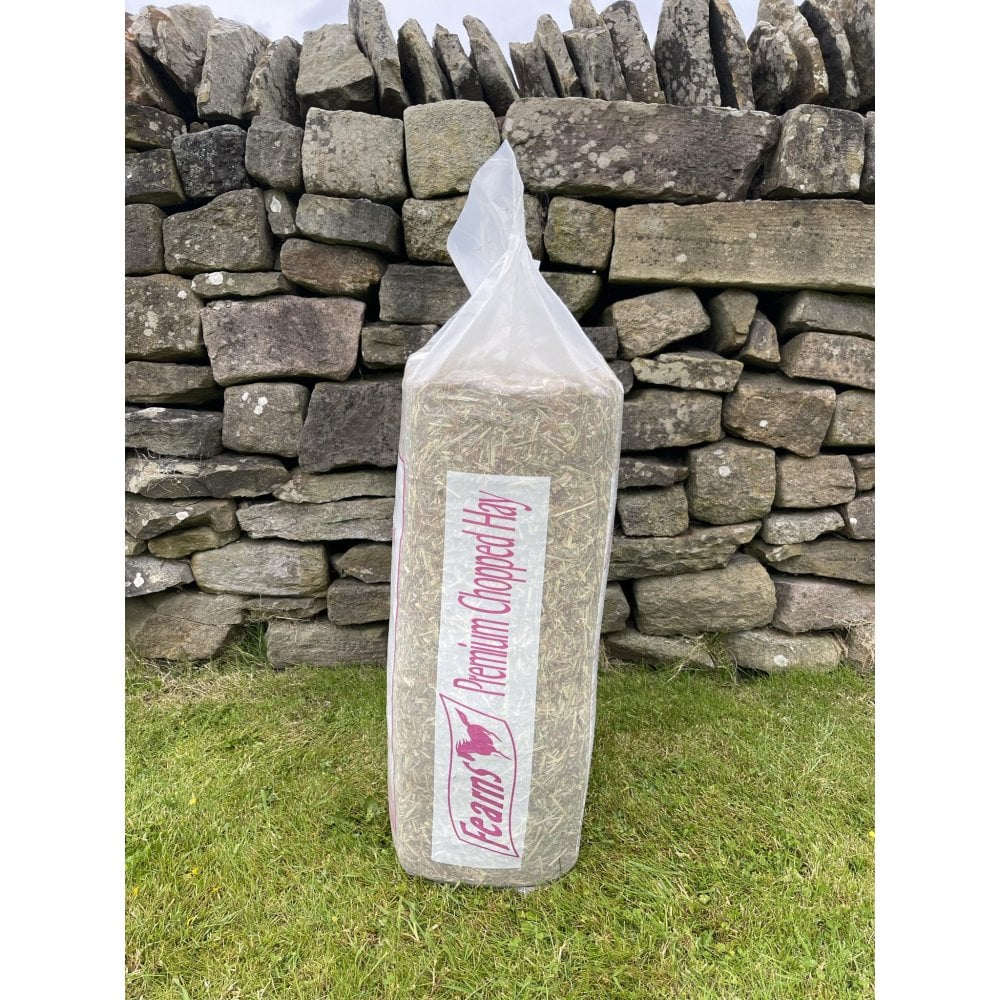 A bag of Fearns Premium Chopped Hay standing upright on grass in front of a rustic stone wall.