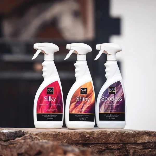 Three NAF spray bottles labeled 'Silky', 'Shiny', and 'Spotless' on a stone surface with a blurred background.