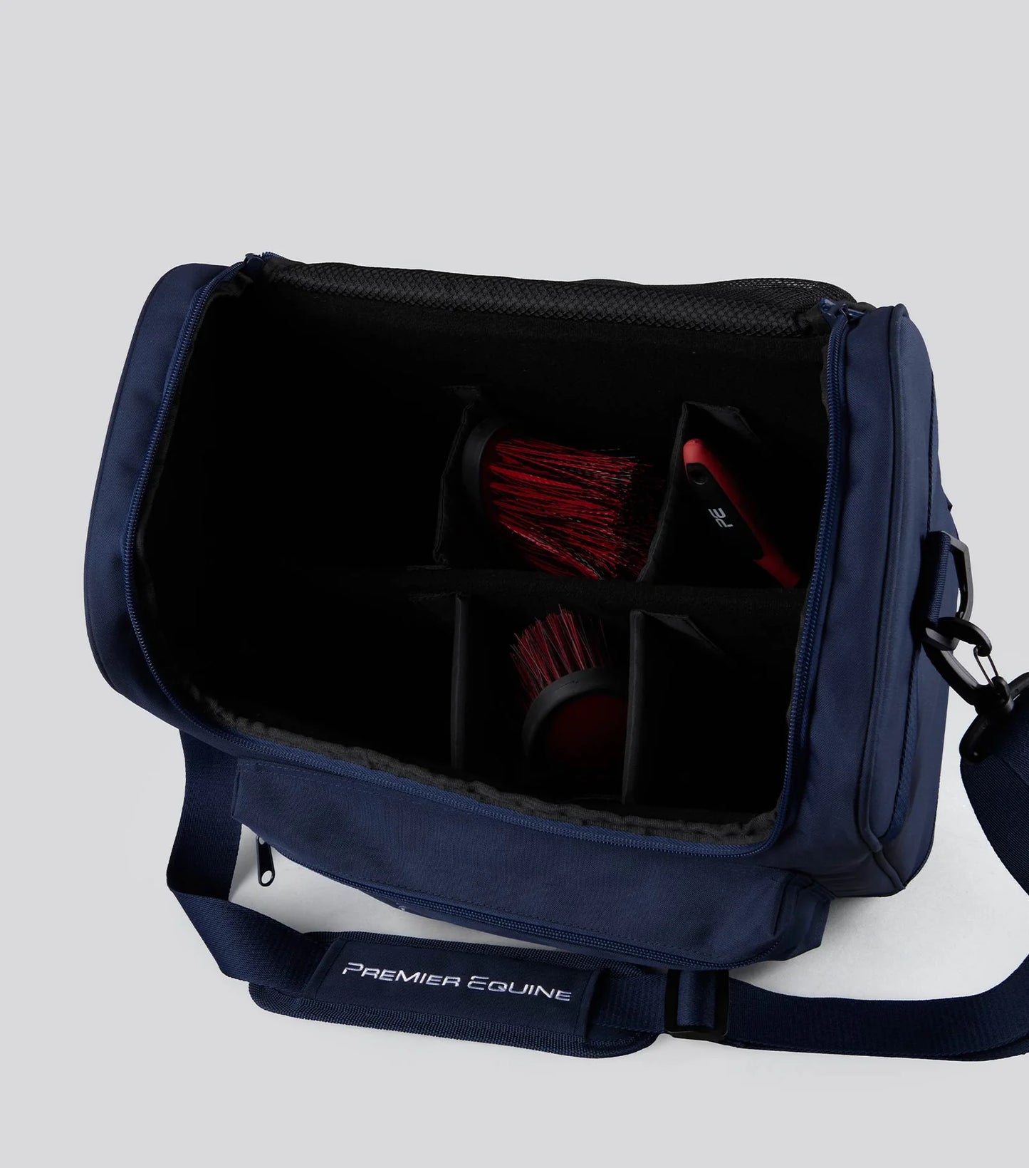 Navy blue grooming bag with red brushes on a light gray background