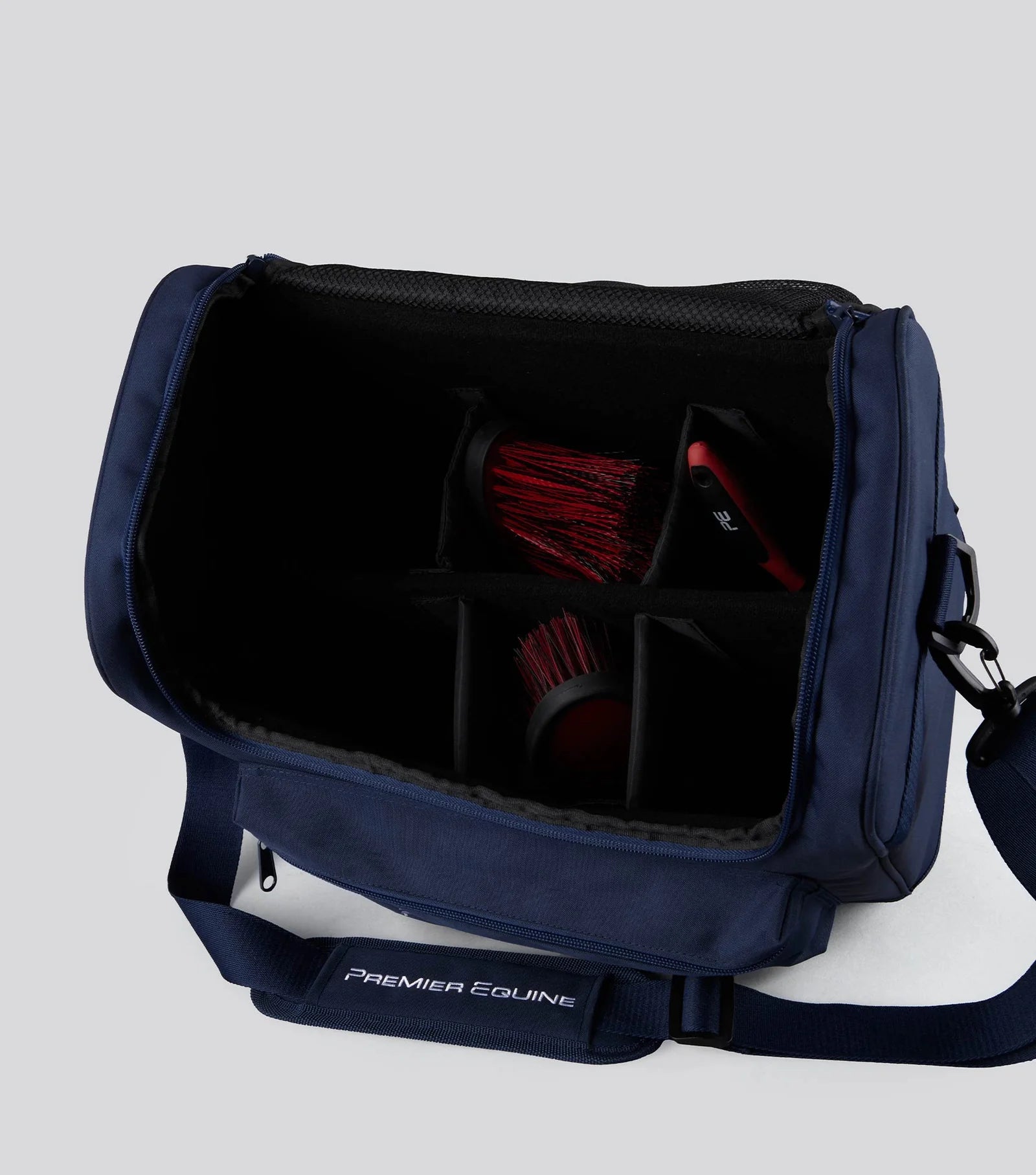 Navy blue grooming bag with red brushes on a light gray background